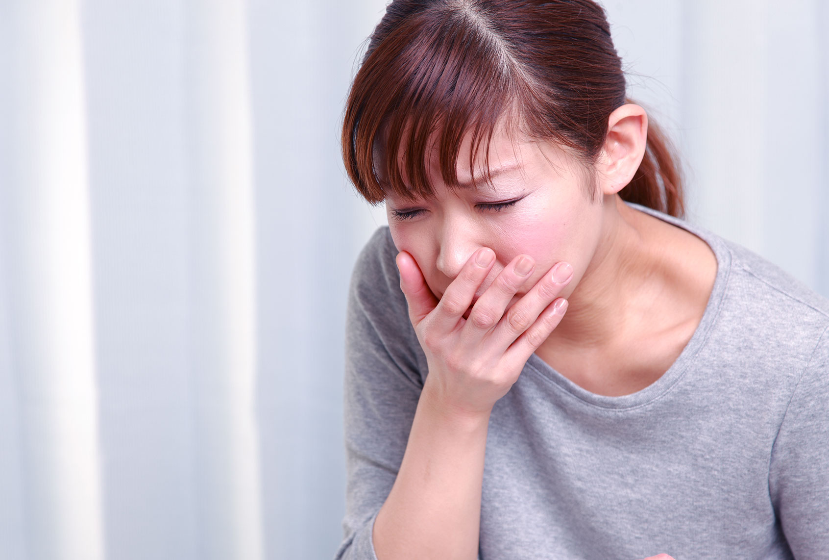 Young woman looking nauseous with hand over mouth (Getty Images)