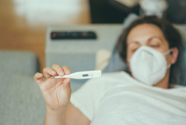 Woman Holding Thermometer While Lying On Bed (Getty Images)