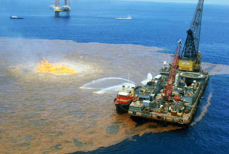 Bay of Campeche, Gulf of Mexico: Workers on barge (right foreground) spray chemical dispersant on excess oil around burning well of the Ixtoc I well here recently. The well continues to gush into the Bay of Campeche, making it the world's largest oil spill. Technicians of Petroleos Mexicanos, the national oil monopoly, last weekend began steadily pumping steel and lead balls--2.5 to 2.7 inches in diameter---into the blown out Ixtoc I well to help lessen the spillage. Through 8/11, Ixtoc I had spewed about 1.81 million barrels of oil into the bay, company officials said. (Getty Images)