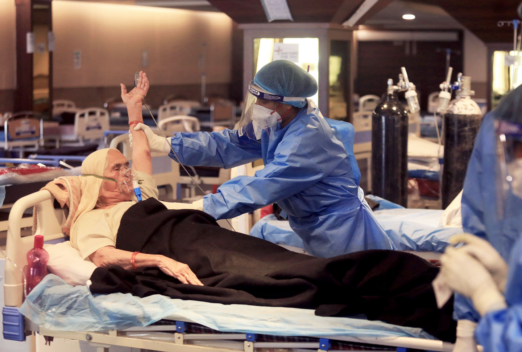 A healthcare worker wearing a personal protective equipment (PPE) attends to Covid-19 patient wearing oxygen mask inside a Covid-19 care center set up at shehnai banquet hall attached with Lok Nayak Jai Prakash Narayan Hospital (LNJP) one of the largest COVID-19 facilities. (Naveen Sharma/SOPA Images/LightRocket via Getty Images)