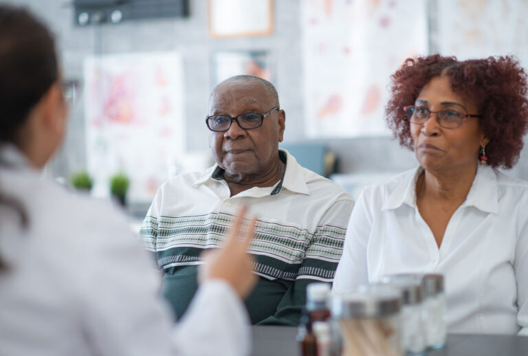 A couple sit next to each other in a doctor's office and listen carefully to their doctor. (Getty Images/FatCamera)
