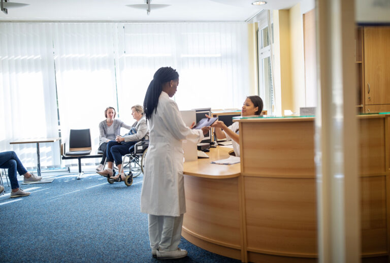 Medical professional at reception with patients waiting in lobby at hospital (Getty Images/Luis Alvarez)