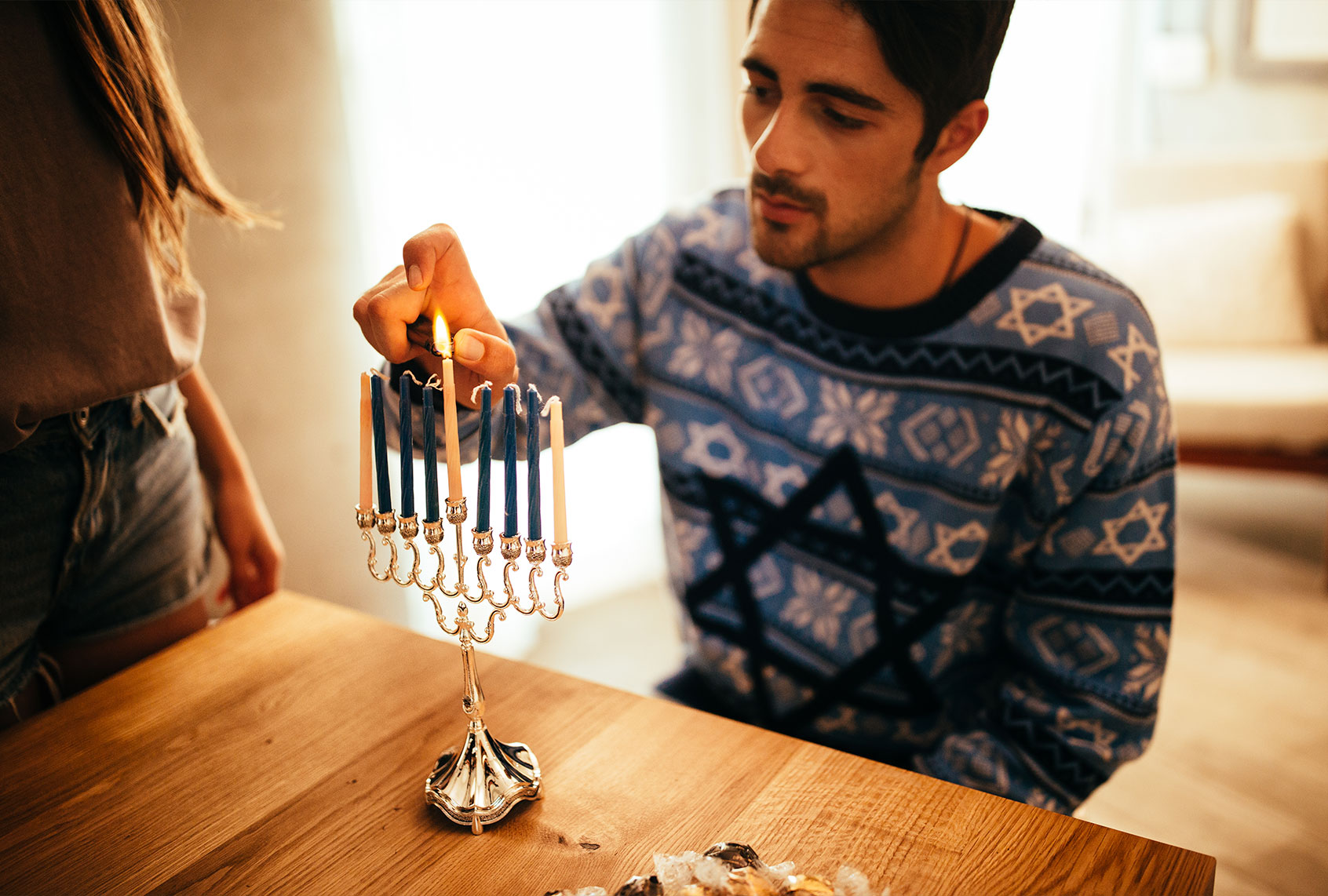 Man wearing a Hanukkah sweater lights a Hanukkah menorah (Getty Image/wundervisuals)