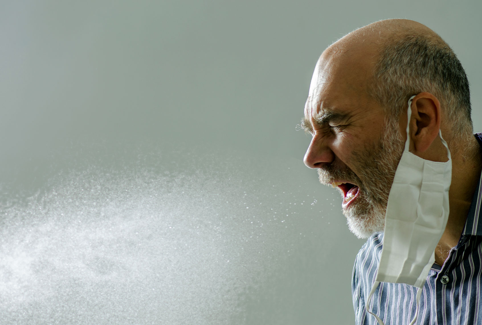 Man sneezing with spray of water droplet full of virus or microbes. He wears his face mask inappropriately on one ear. (Getty Images/Marc Dufresne)