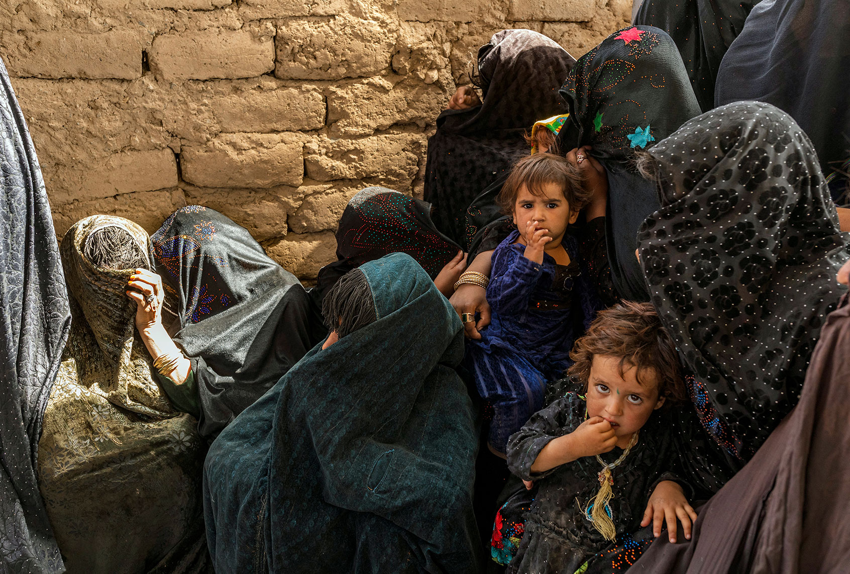 Afghan families gather at the Distribution site of WFP Special Nutritious Food to Pregnant and Lactating Mothers with Acute Malnutrition (AM PLW) and Children aged 6-59 months with moderate Acute Malnutrition (MAM children) at an Internally Displaced Camp on September 29, 2021, in the outskirt of Herat, Afghanistan. Since the Taliban retook control of Afghanistan in August 2021, the economy has suffered after the world aid funding stopped, which has created a humanitarian crisis. Most art, culture, and pastimes have been banned. The female population has also had to quit jobs and young girls after the age of 12 can no longer go to school or further education. (Marco Di Lauro/Getty Images)