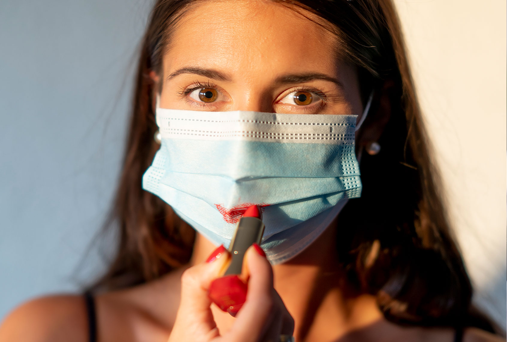 Young woman painting her lips red over a face mask (Getty Images/Cavan Images)