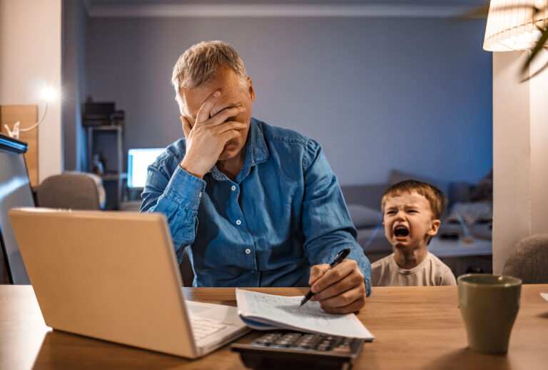 Busy mature businessman working from home and watching his crying son at night, who is is yelling at him. (Getty Images;ljubaphoto)