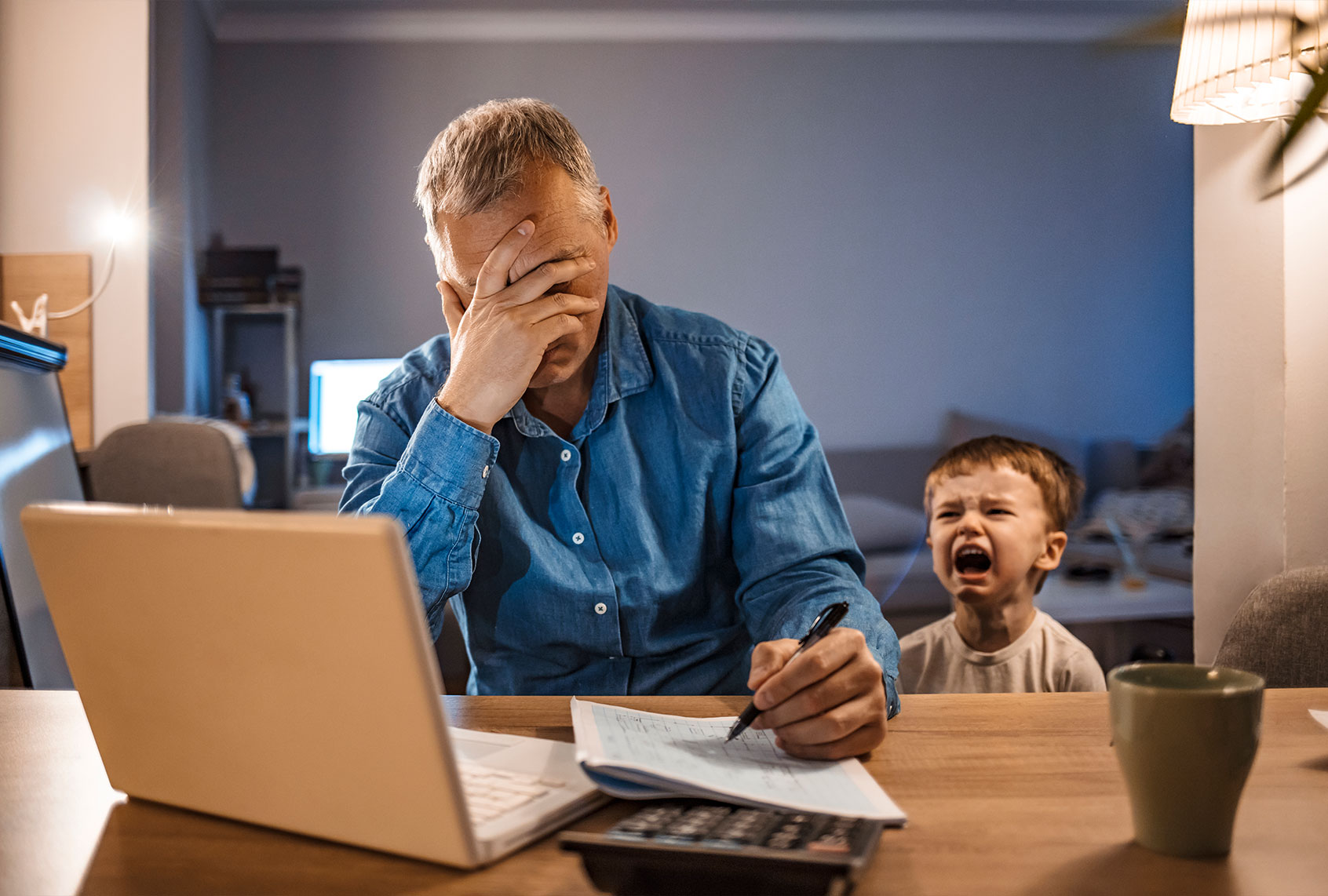 Busy mature businessman working from home and watching his crying son at night, who is is yelling at him. (Getty Images;ljubaphoto)
