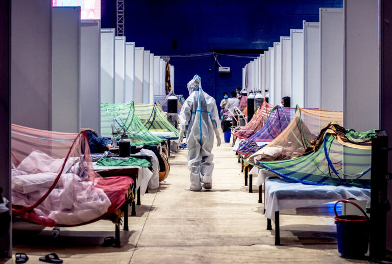 A medical worker in PPE observes patients who have been infected by Covid-19 inside a makeshift covid care facility in a sports stadium at the Commonwealth Games Village in New Delhi, India. (Getty Images/Stringer)