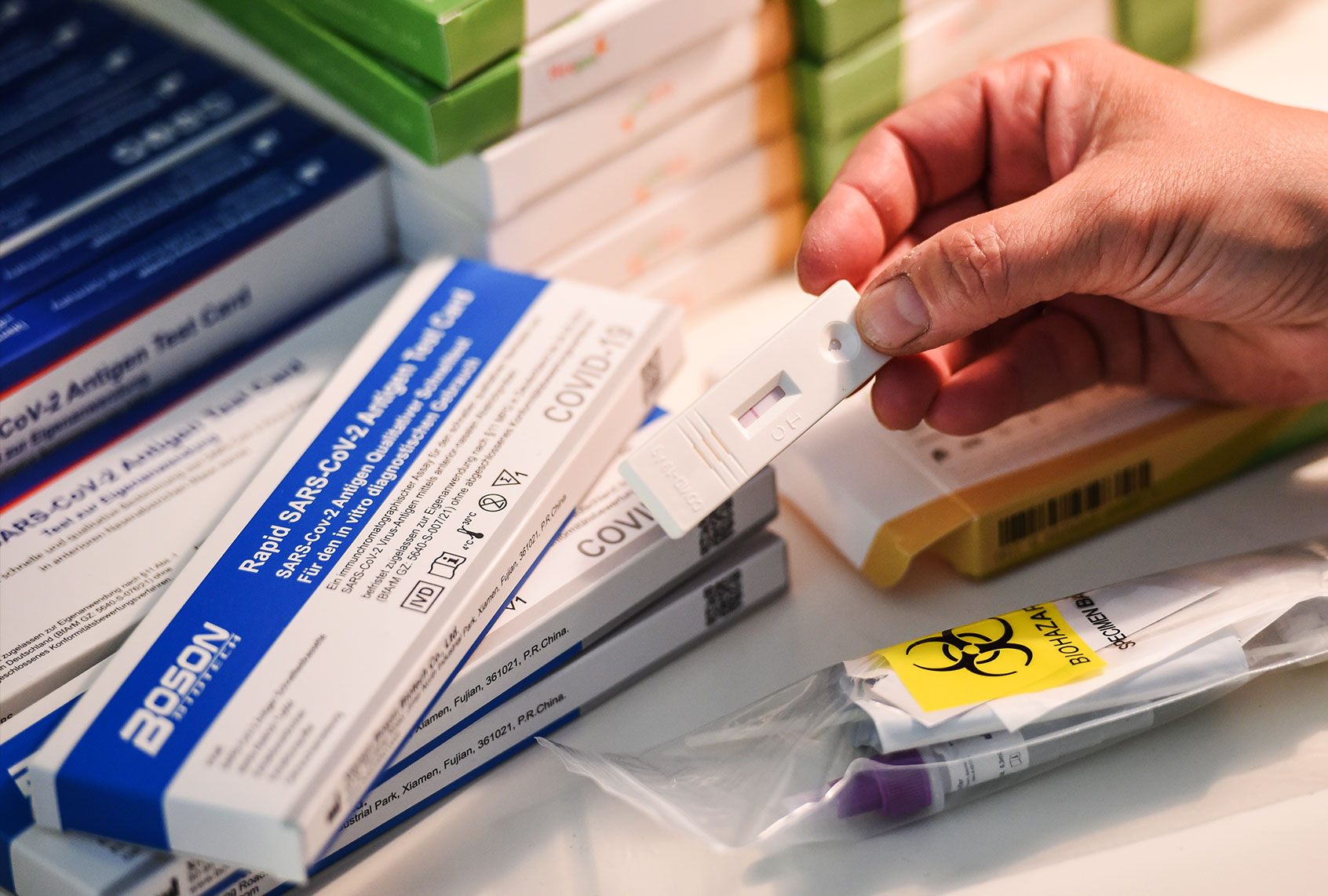 A woman holds a Corona test cassette indicating a preliminary negative result. In the background, several Corona self-tests lie on a table. (Kira Hofmann/picture alliance via Getty Images)