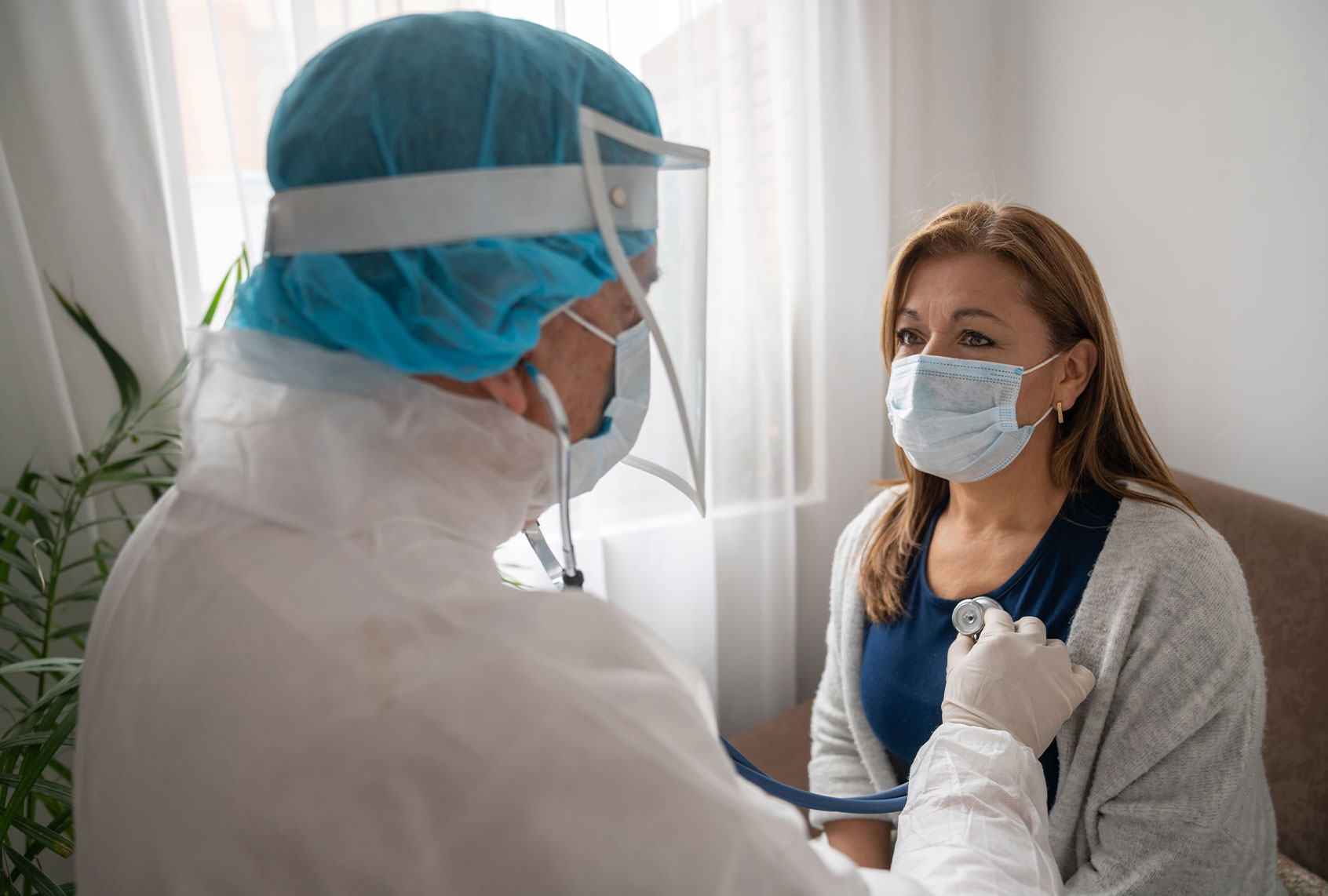 Doctor examining a woman at home and listening to her chest with a stethoscope (Getty Images/Hispanolistic)