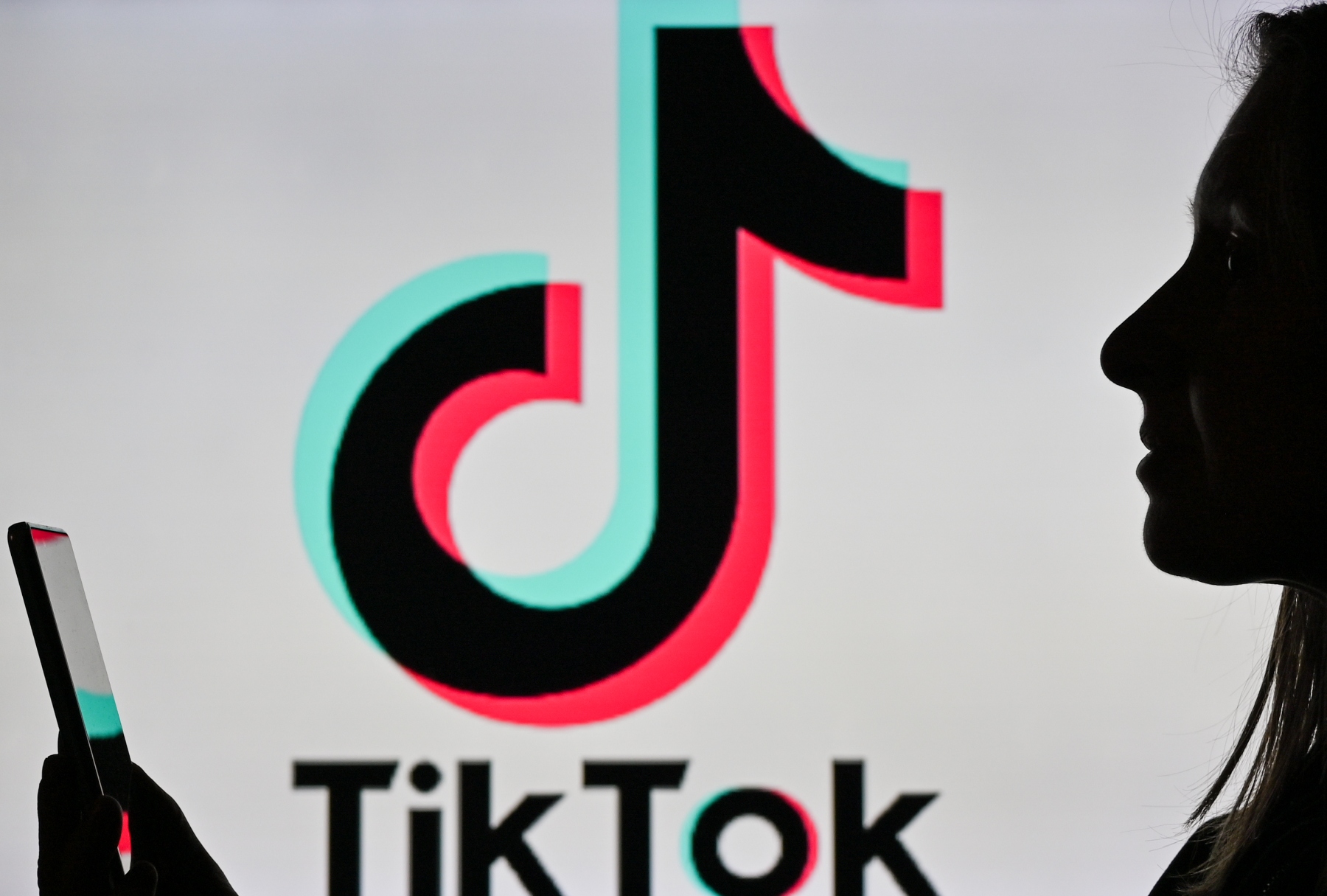 Silhouette of woman looking at phone and Tiktok ( Artur Widak/NurPhoto via Getty Images)