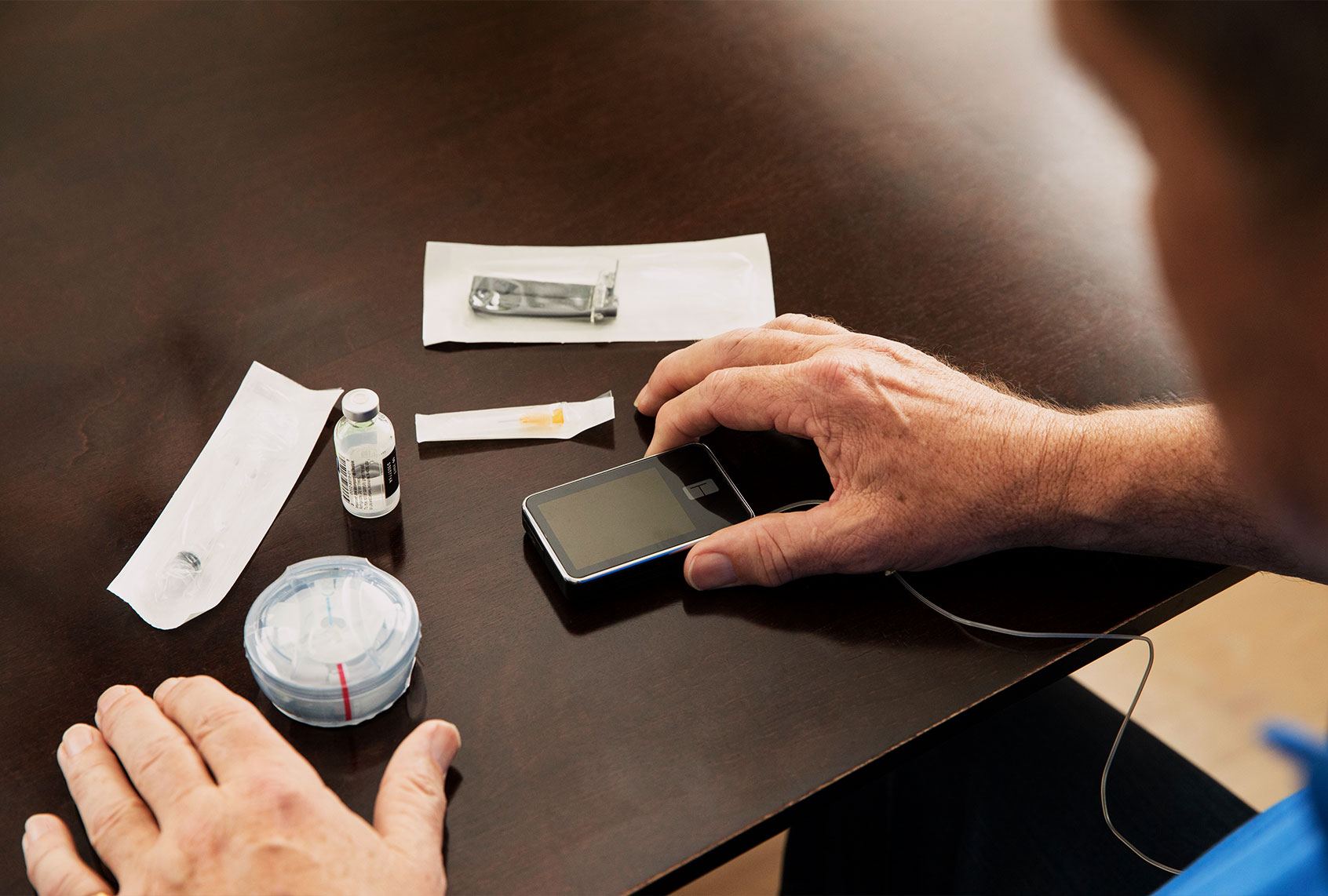 In this photo illustration, a man looks at his supplies for type-1 diabetes management, including tubed insulin pump, insulin vial, syringe, needle, insulin cartridge, and infusion site applicator. (Matt Harbicht/Getty Images for Tandem Diabetes Care)