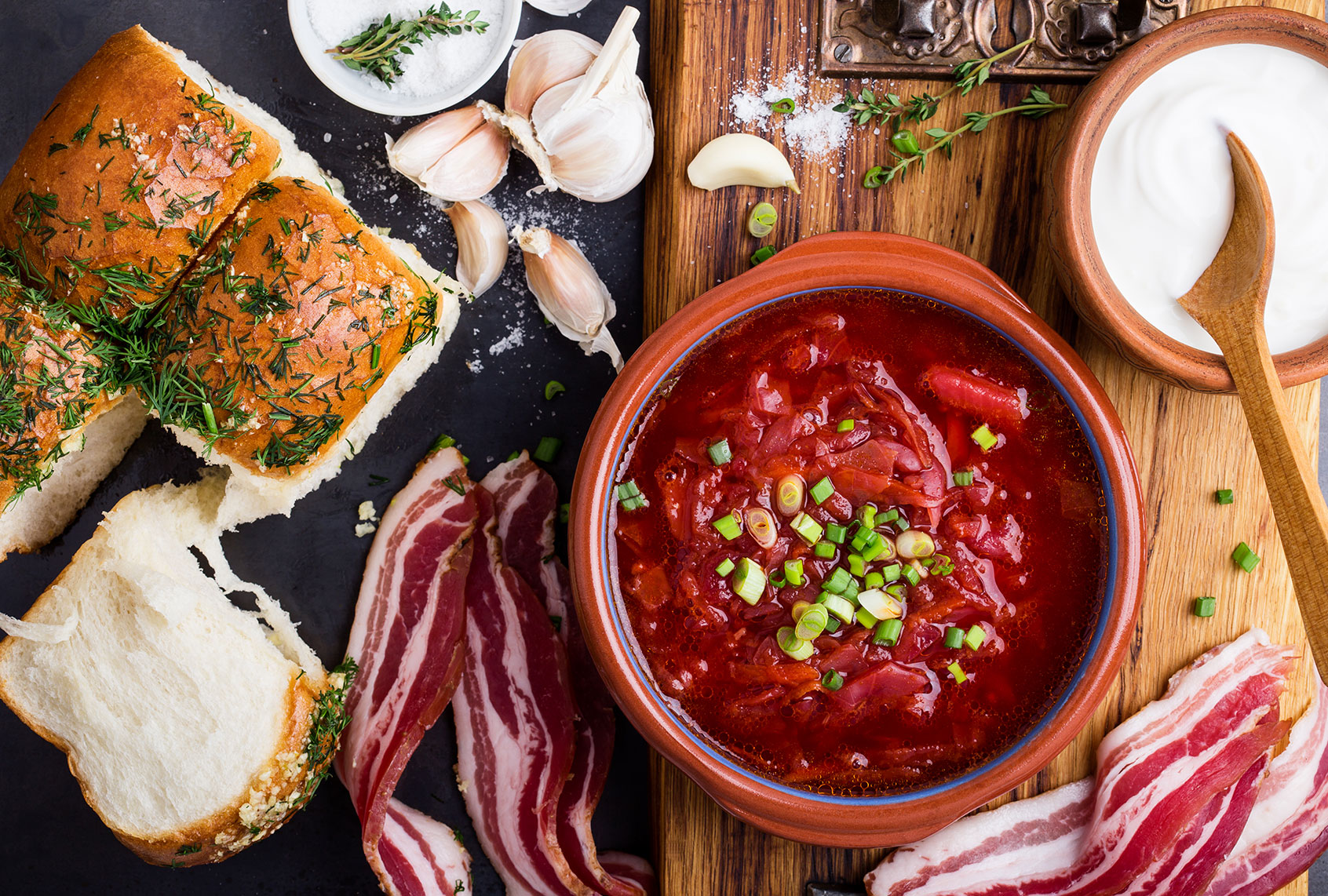 Red beet soup borscht in ceramic bowl with garlic buns pampushka and dry cured pork belly on rustic table (Getty Images/istetiana)