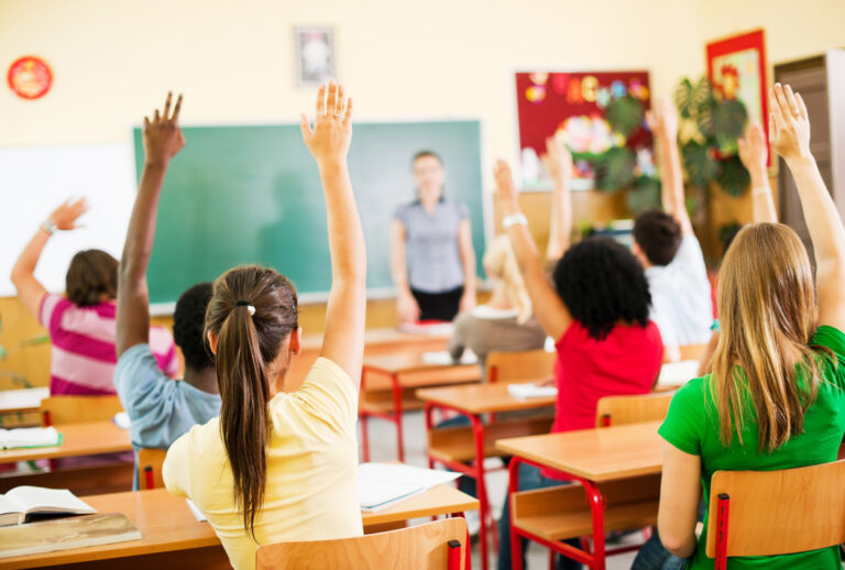 Students sitting in a classroom and raising hands (Getty Images / skynesher)