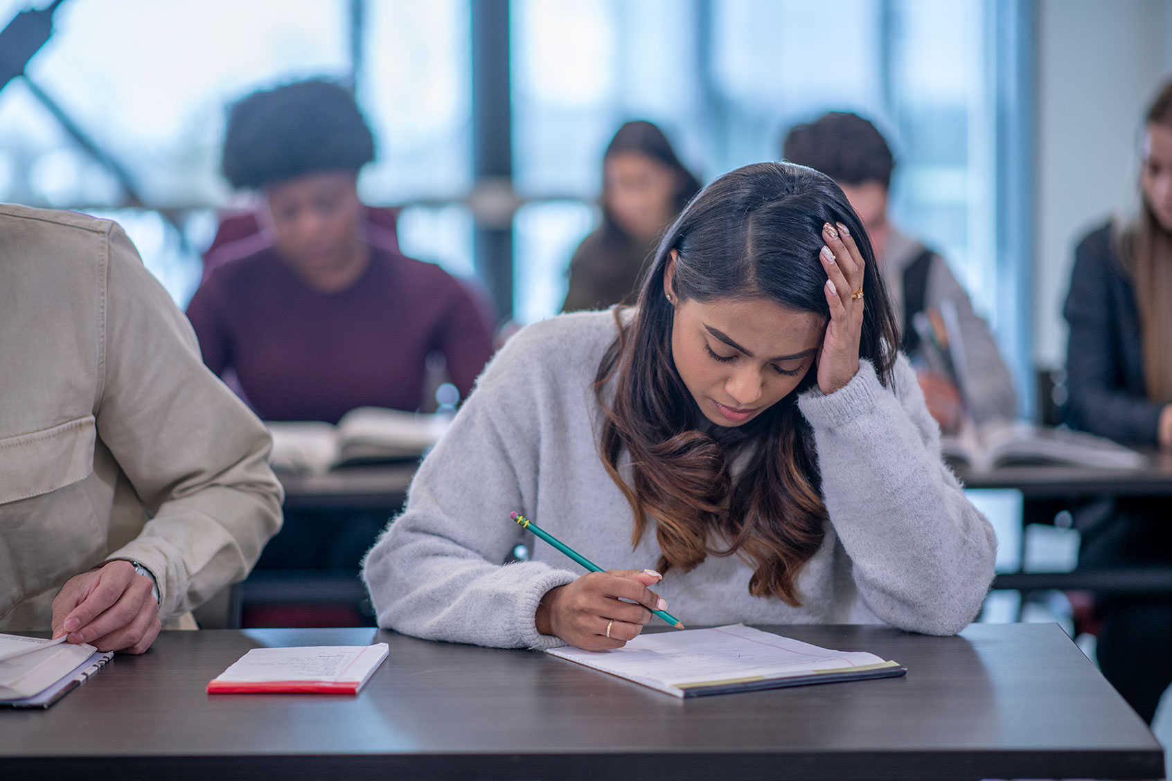 A young woman sits at her desk and takes notes. She has her head in her hand in concentration. (Getty Images/FatCamera)