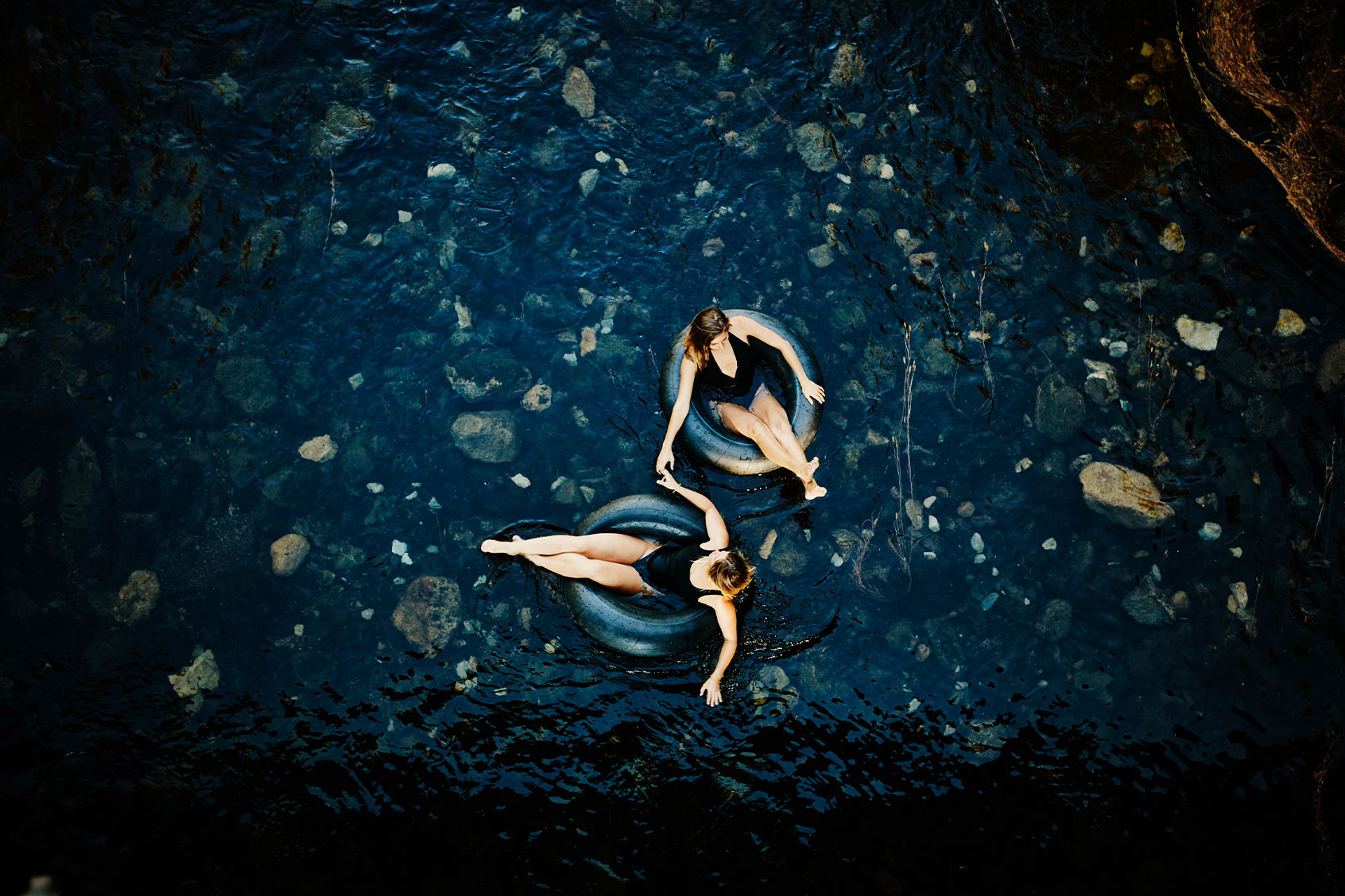 Two women holding hands floating in inner tubes on the river on a summer evening (Getty Images/Thomas Barwick)