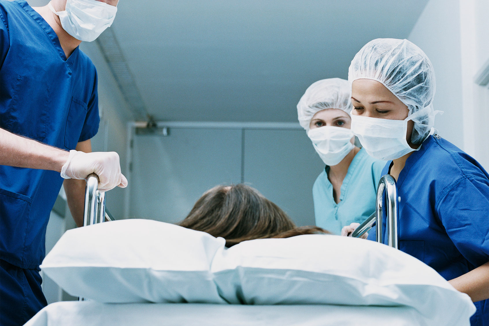 Surgeons in Scrubs and Protective Masks Look Down at a Patient on a Hospital Trolley (Getty Images/Janie Airey)