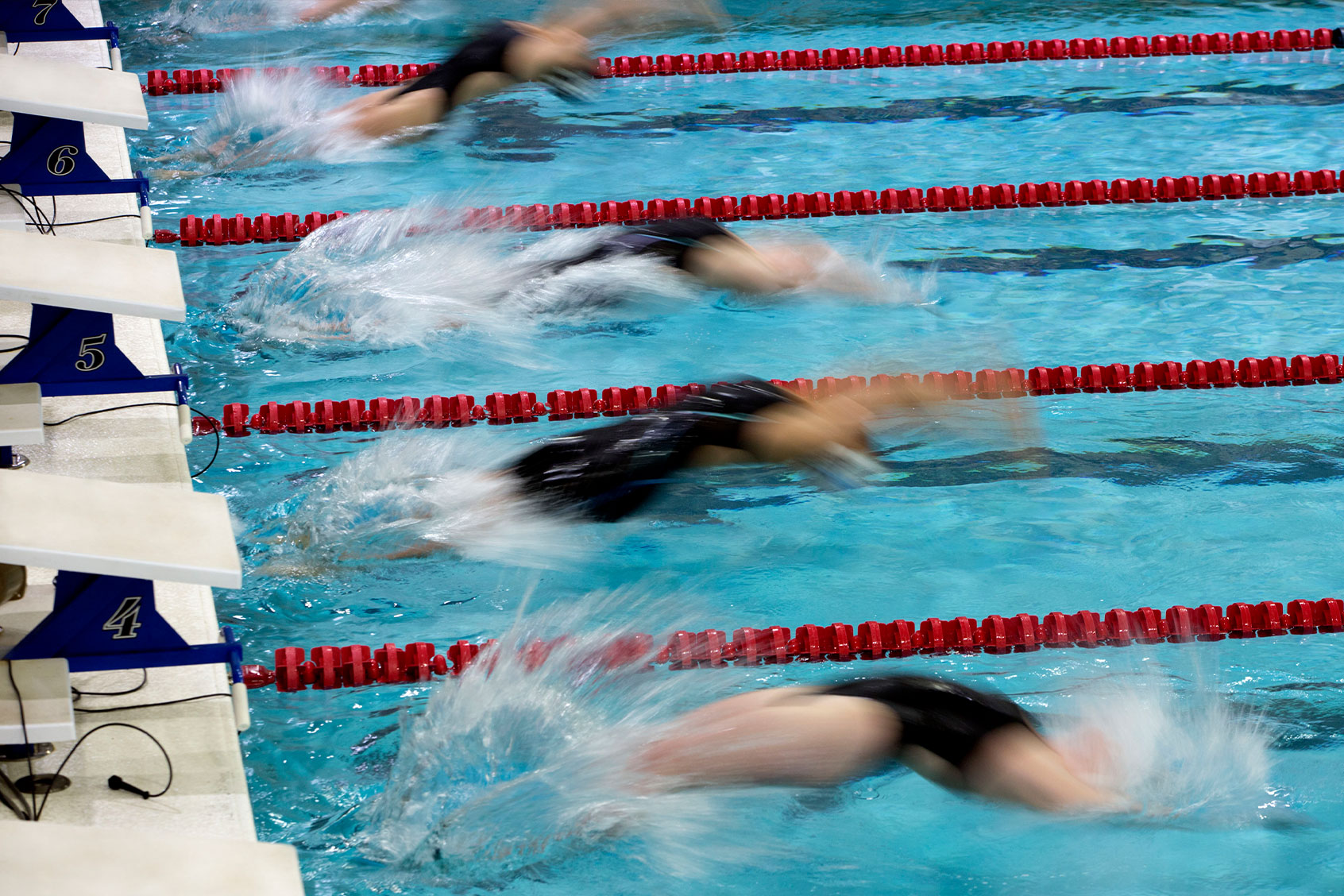 Motion view of girl backstroke swimmers starting a race and entering the water together (Getty Images/Jonathan Kirn)