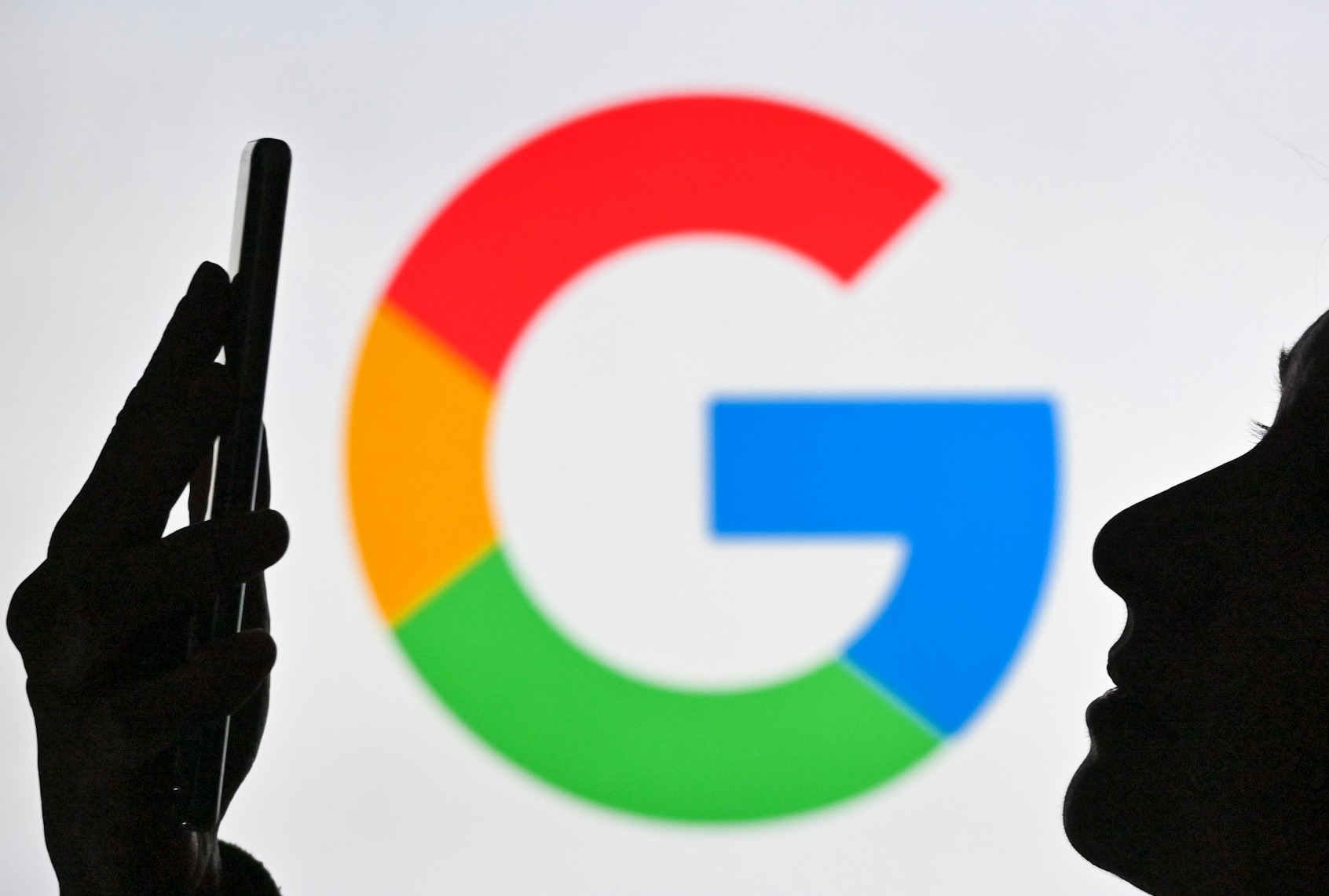 A woman holding a cell phone in front of the Google logo displayed on a computer screen. (Artur Widak/NurPhoto via Getty Images)