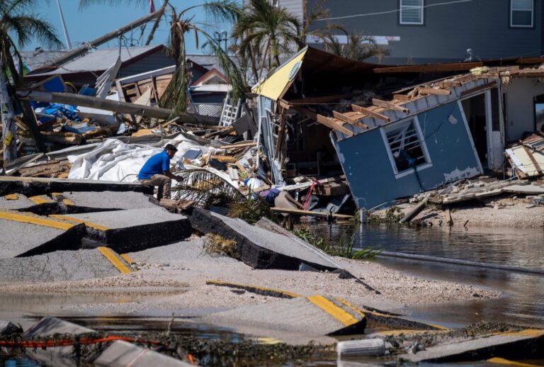 A man sits on a broken section of the Pine Island Road in the aftermath of Hurricane Ian in Matlacha, Florida on October 1, 2022. (RICARDO ARDUENGO/AFP via Getty Images)