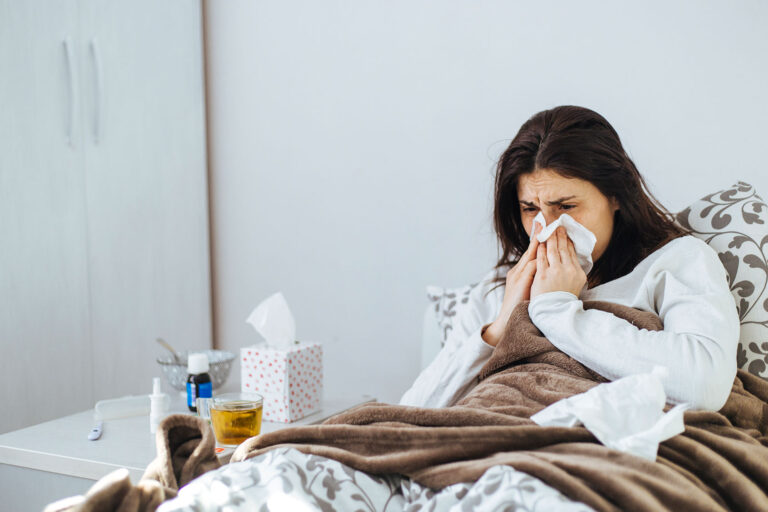 Sick Woman Lying In Bed With Tissues (Getty Images/Obradovic)