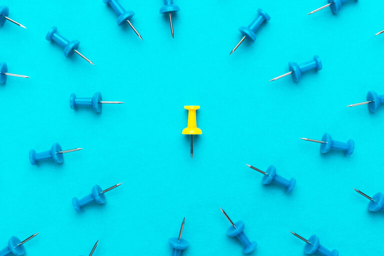 Yellow push pin in the center of blue push pins with their spike turned to the yellow one (Getty Images/loongar)