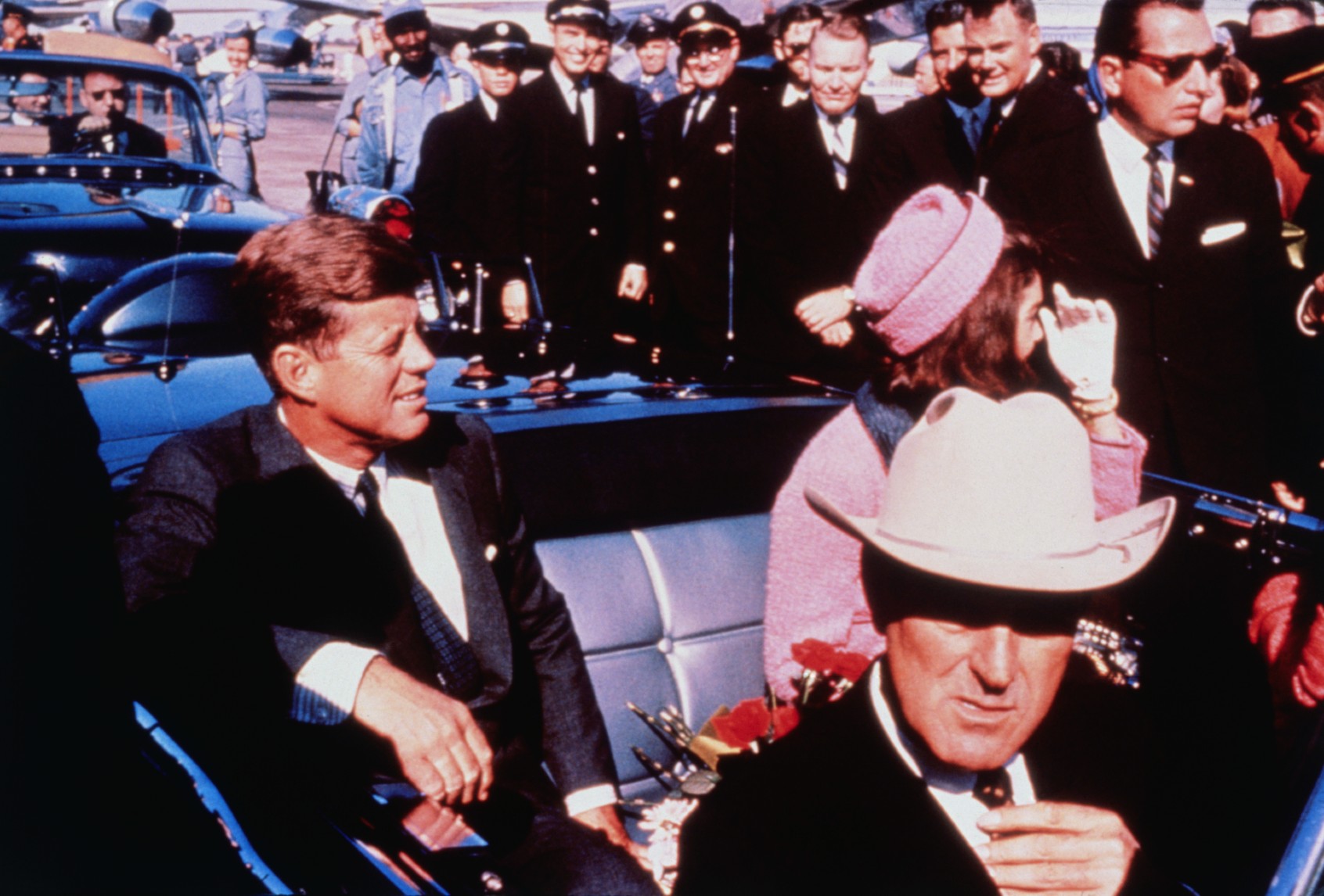Texas Governor John Connally adjusts his tie (foreground) as US President John F Kennedy (left) & First Lady Jacqueline Kennedy (in pink) settled in rear seats, prepared for motorcade into city from airport, Nov. 22. After a few speaking stops, the President was assassinated in the same car. (Bettmann / Contributor/Getty)