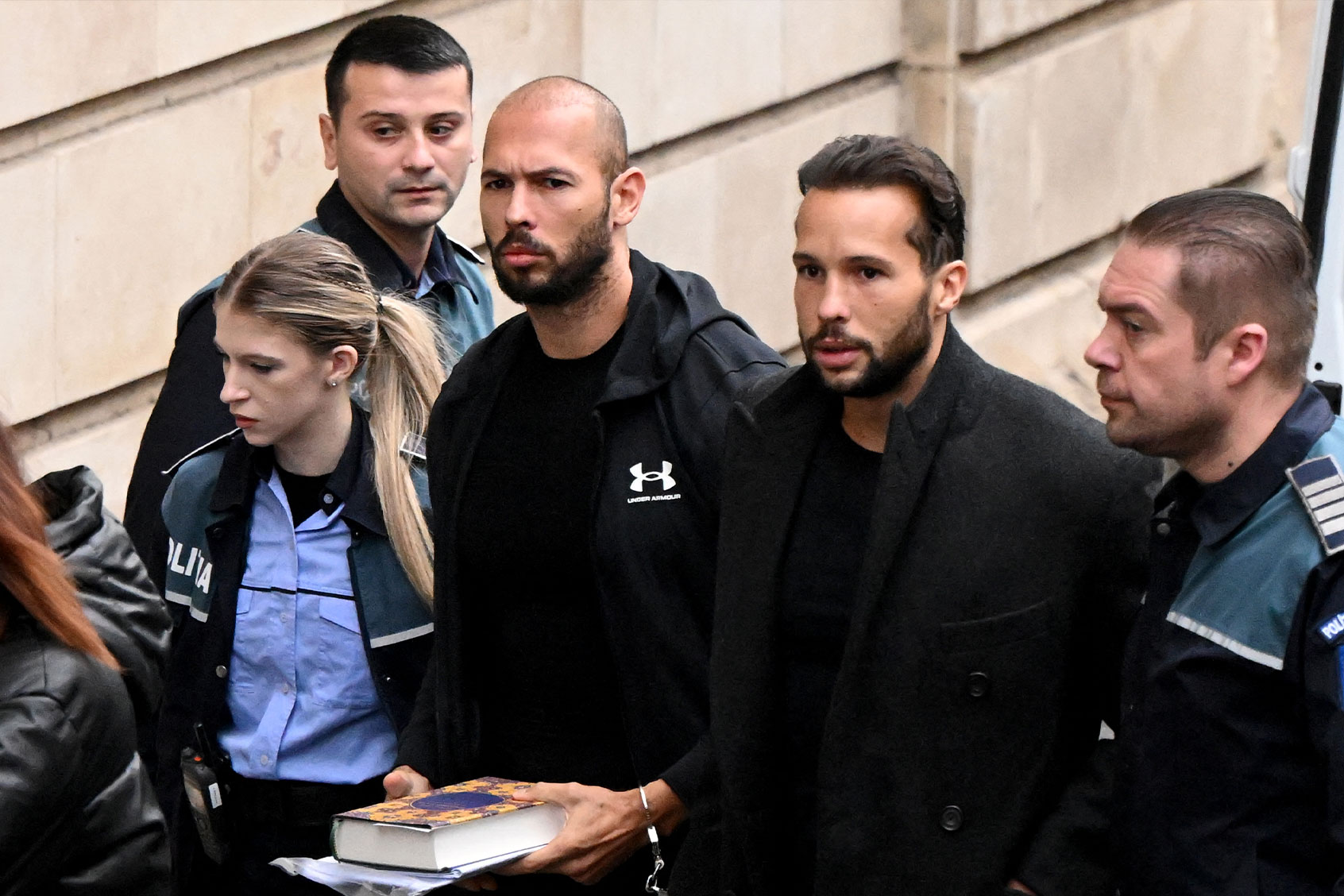 British-US influencer Andrew Tate (3rd R) and his brother Tristan Tate (2nd R) arrive handcuffed and escorted by police at a courthouse in Bucharest on January 10, 2023 for a court hearing on their appeal against pre-trial detention for alleged human trafficking, rape and forming a criminal group. (DANIEL MIHAILESCU/AFP via Getty Images)