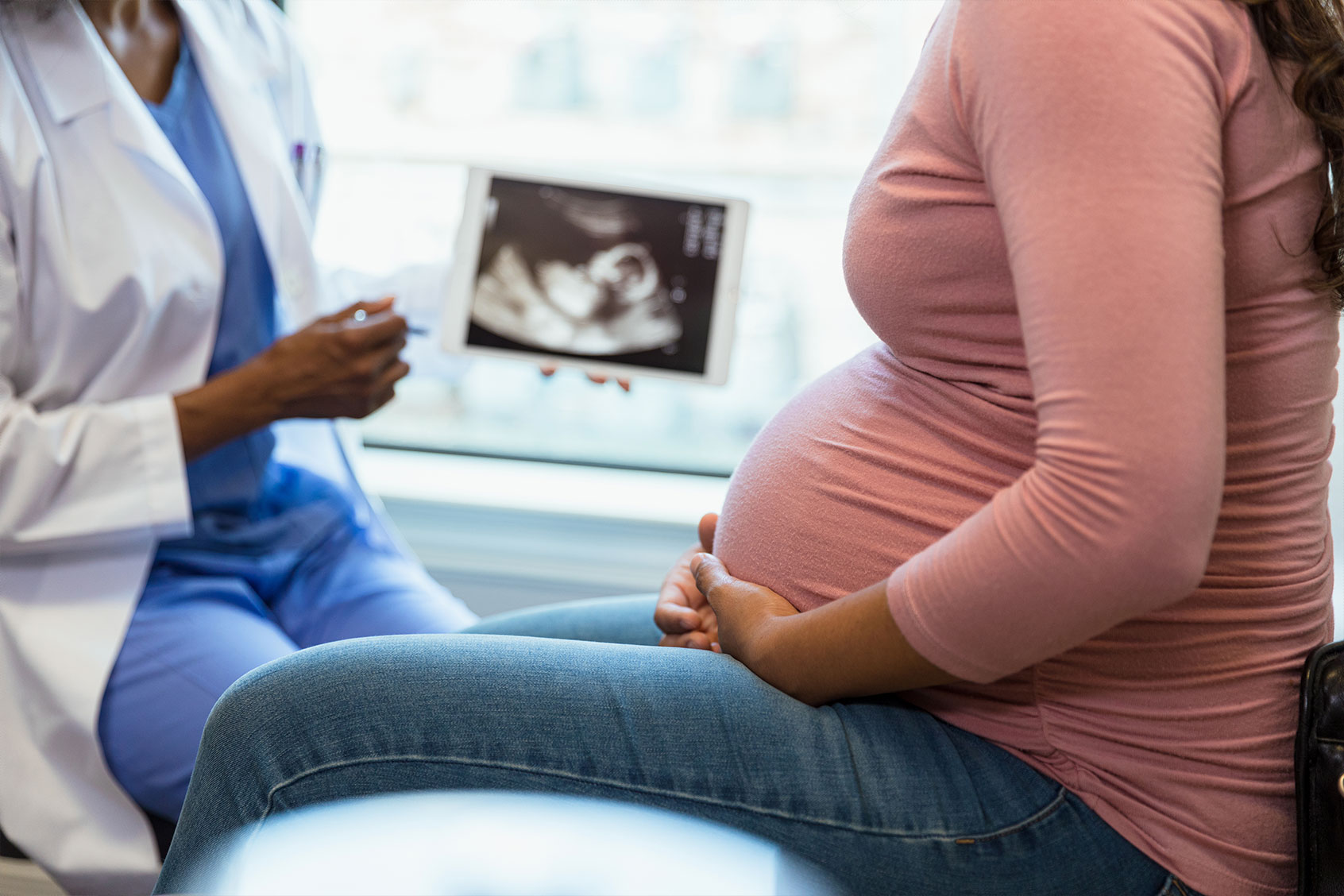 A pregnant woman in the foreground as the unrecognizable doctor shows her an ultrasound (Getty Images/SDI Productions)