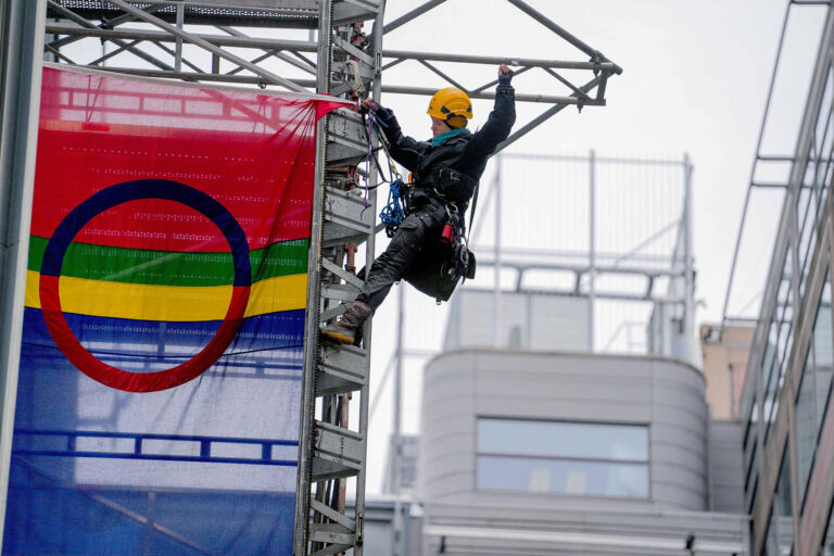 An activist hangs the Sami flag on a scaffolding next to the Ministry of Oil and Energy during an action staged on March 2, 2023 in Oslo, in a protest against wind turbines built on land traditionally used to herd reindeer. (JAVAD PARSA/NTB/AFP via Getty Images)