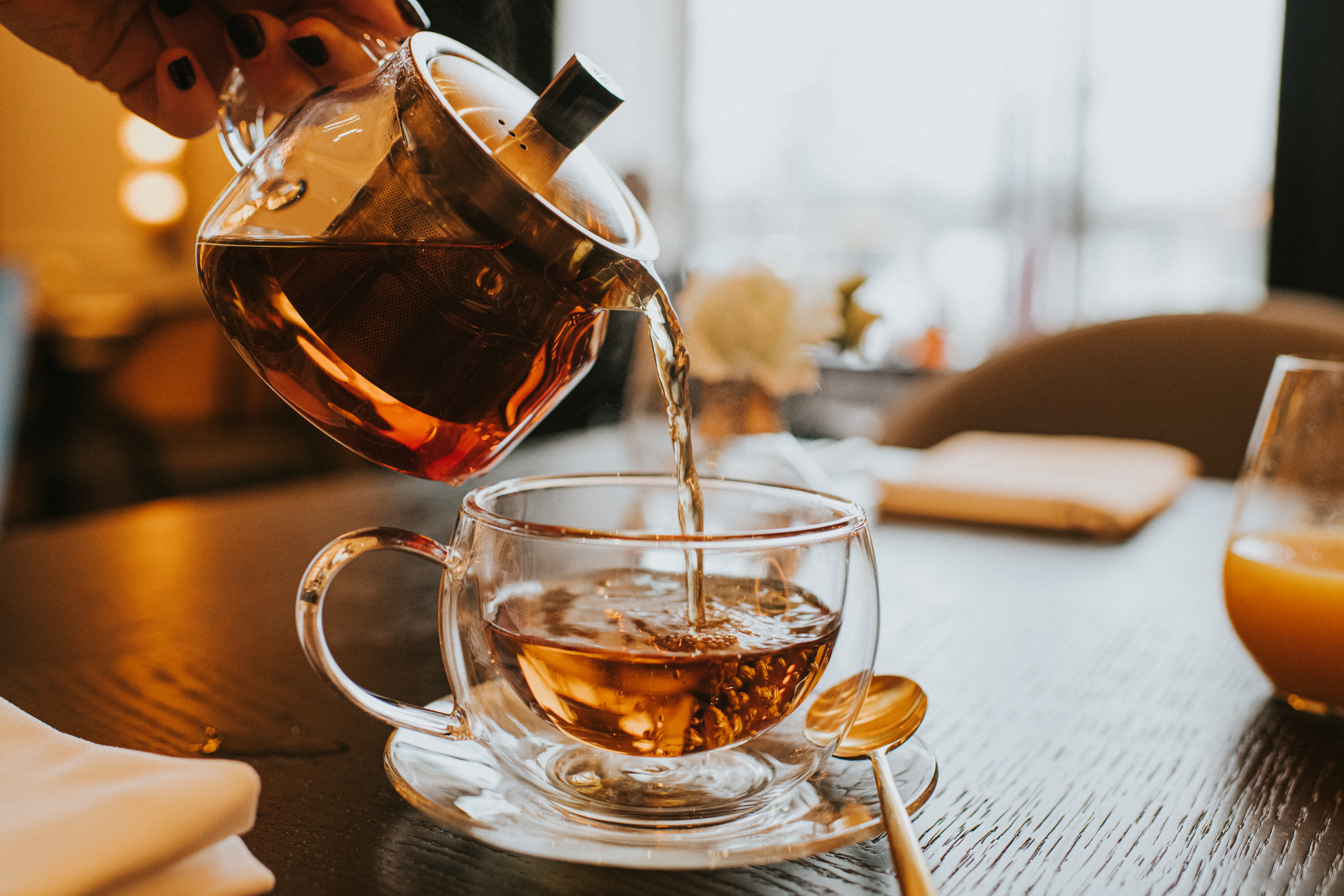 Hand pouring a cup of tea from a stylish transparent teapot into a clear cup. (Catherine Falls Commercial/Getty Images)