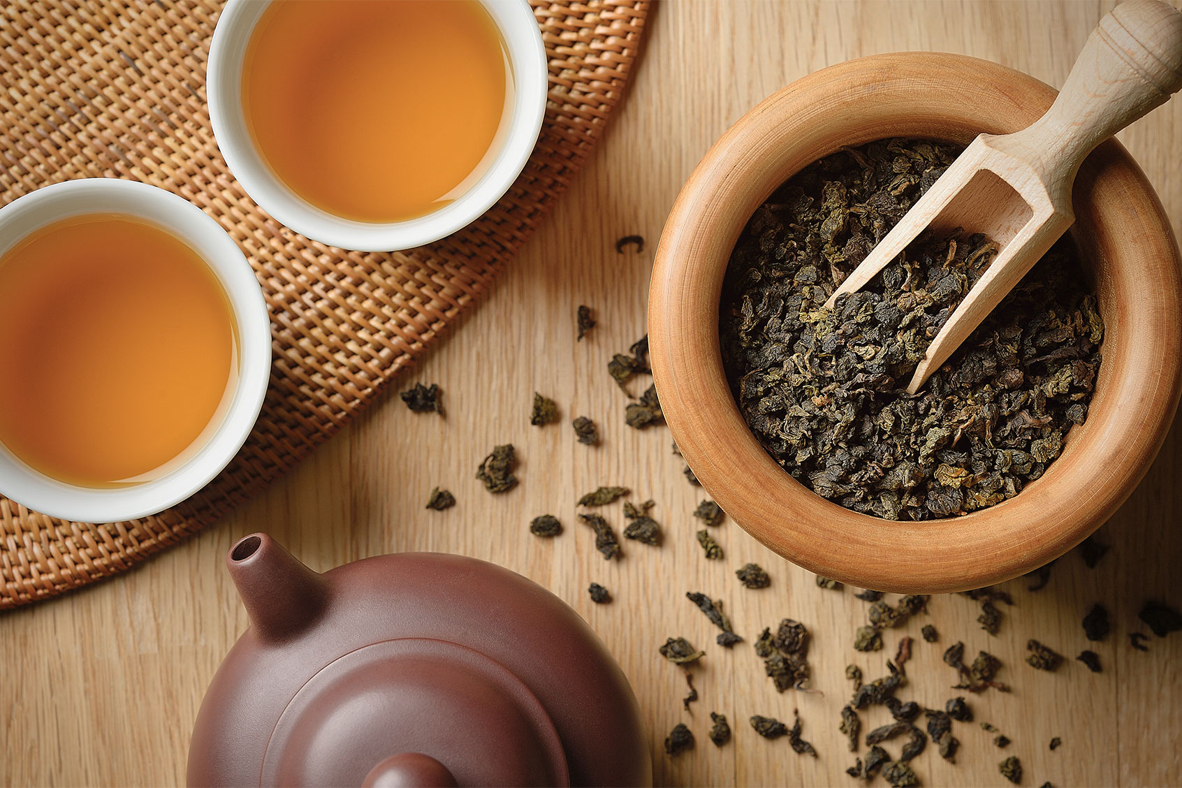 Tea leaves spilling out from wooden bowl, near freshly brewed Oolong tea (Getty Images/Yagi Studio)