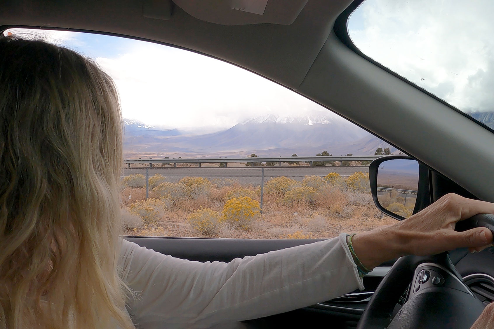 Woman drives her car down a desert road, looking off into the distance (Getty Images/AscentXmedia)