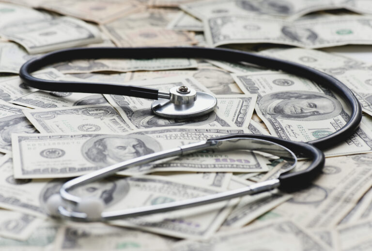 Stethscope on pile of US banknotes (PhotoAlto/Odilon Dimier via Getty Images)