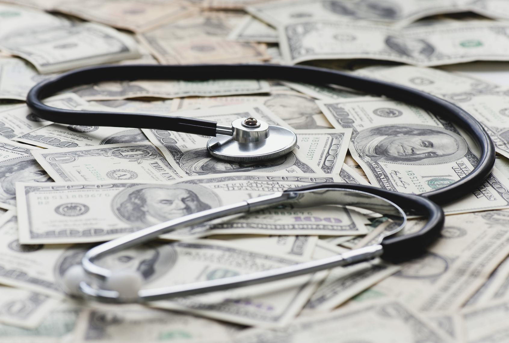 Stethscope on pile of US banknotes (PhotoAlto/Odilon Dimier via Getty Images)