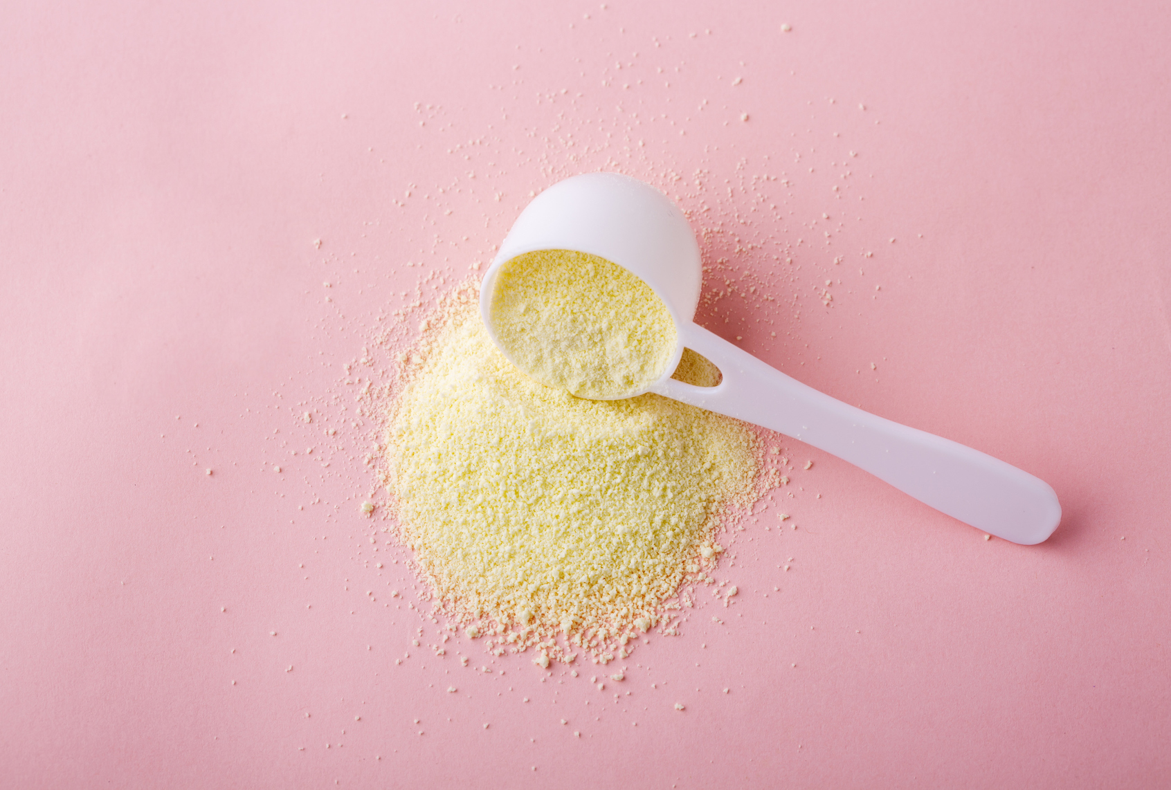 Powdered milk in plastic spoon on pink background (HUIZENG HU via Getty Images)