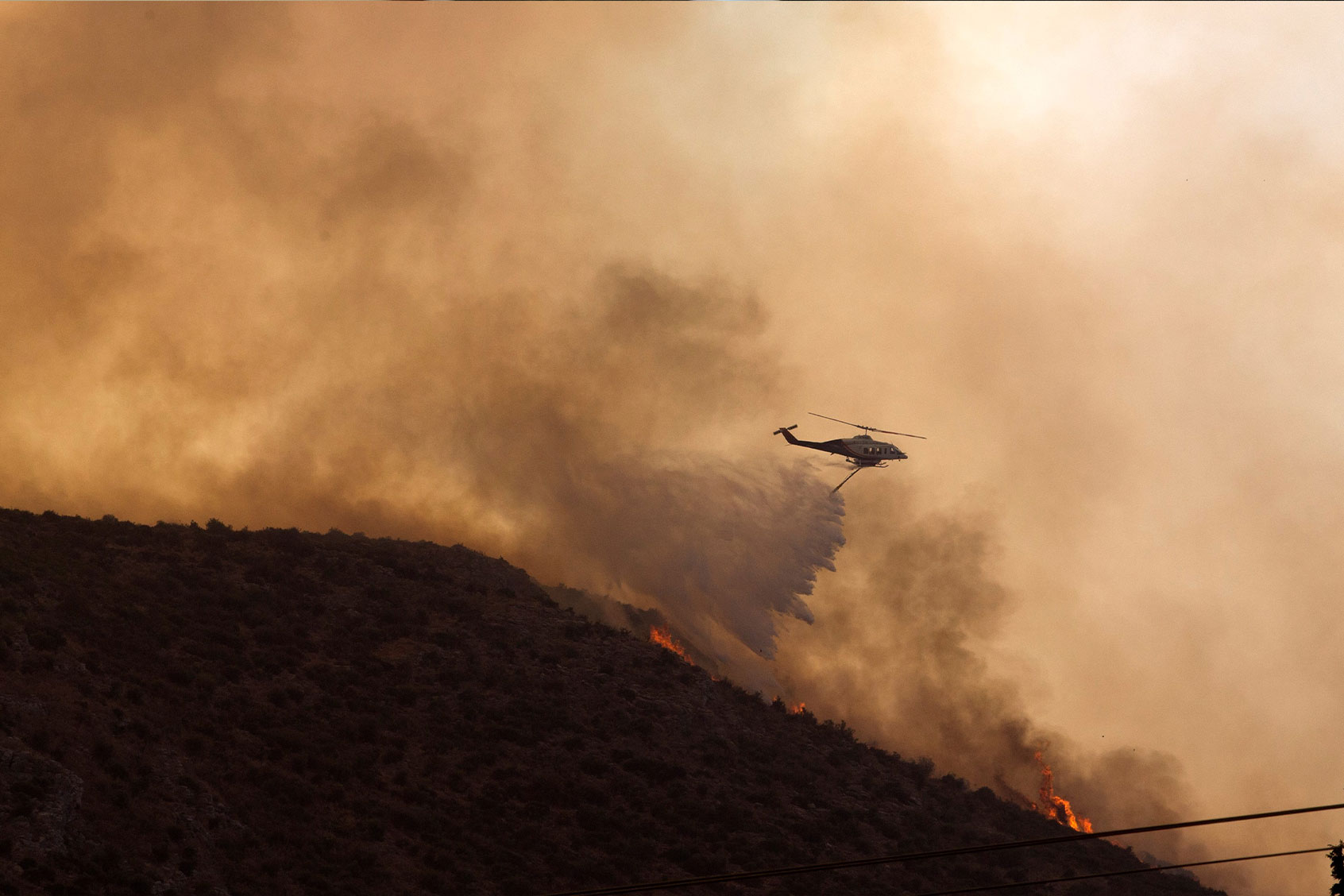 A firefighting helicopter douses a wildfire in Nea Anchialos town, Volos, Greece, on July 27, 2023. (Marios Lolos/Xinhua via Getty Images)