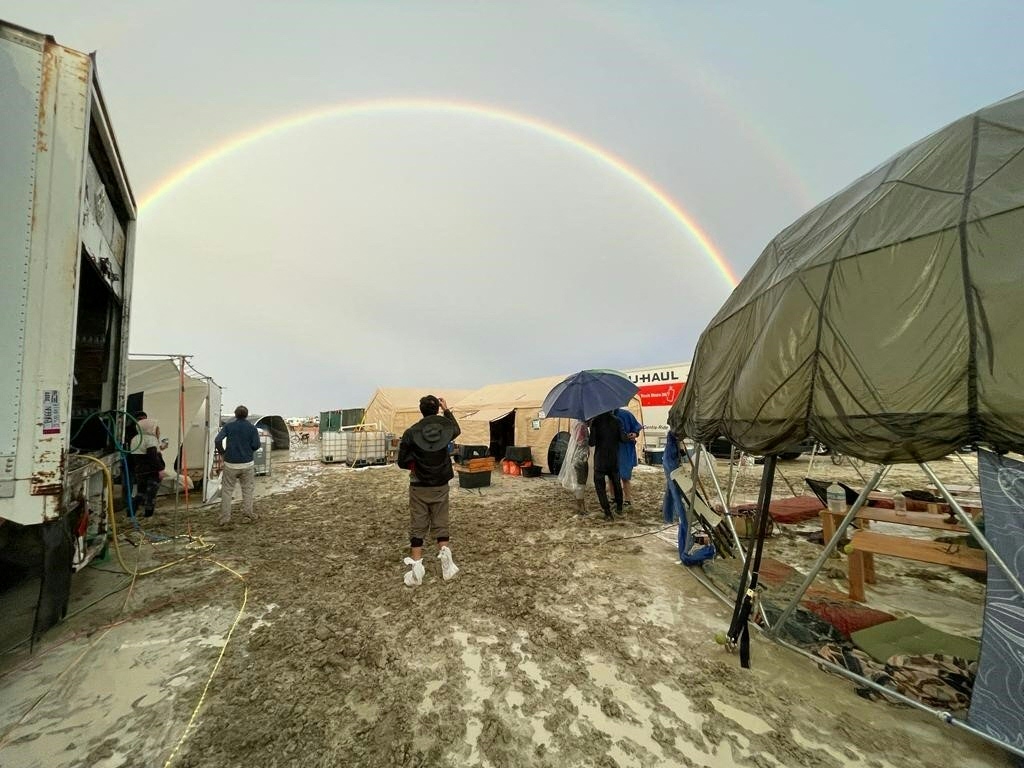 Attendees look at a rainbow over flooding on a desert plain on September 1, 2023, after heavy rains turned the annual Burning Man festival site in Nevada's Black Rock desert into a mud pit. (Photo by JULIE JAMMOT/AFP via Getty Images)