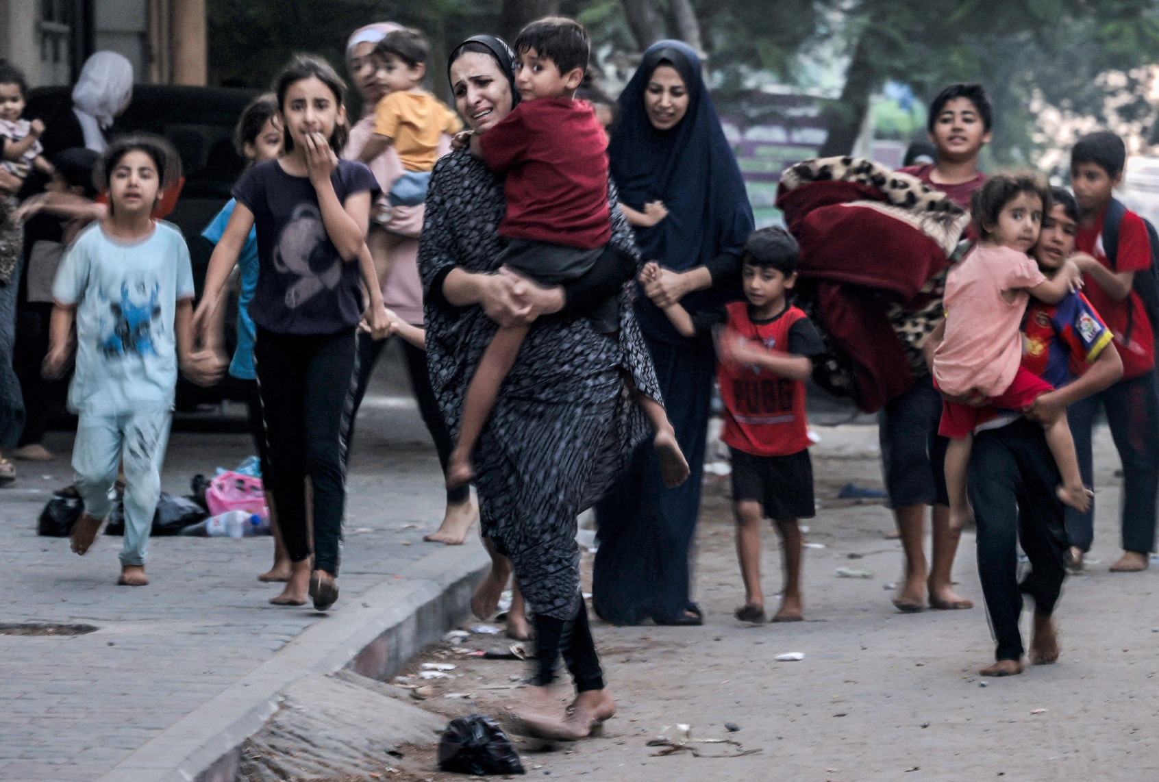 Palestinian women with their children fleeing from their homes following Israeli air strikes rush along a street in Gaza City on October 11, 2023. (MOHAMMED ABED/AFP via Getty Images)