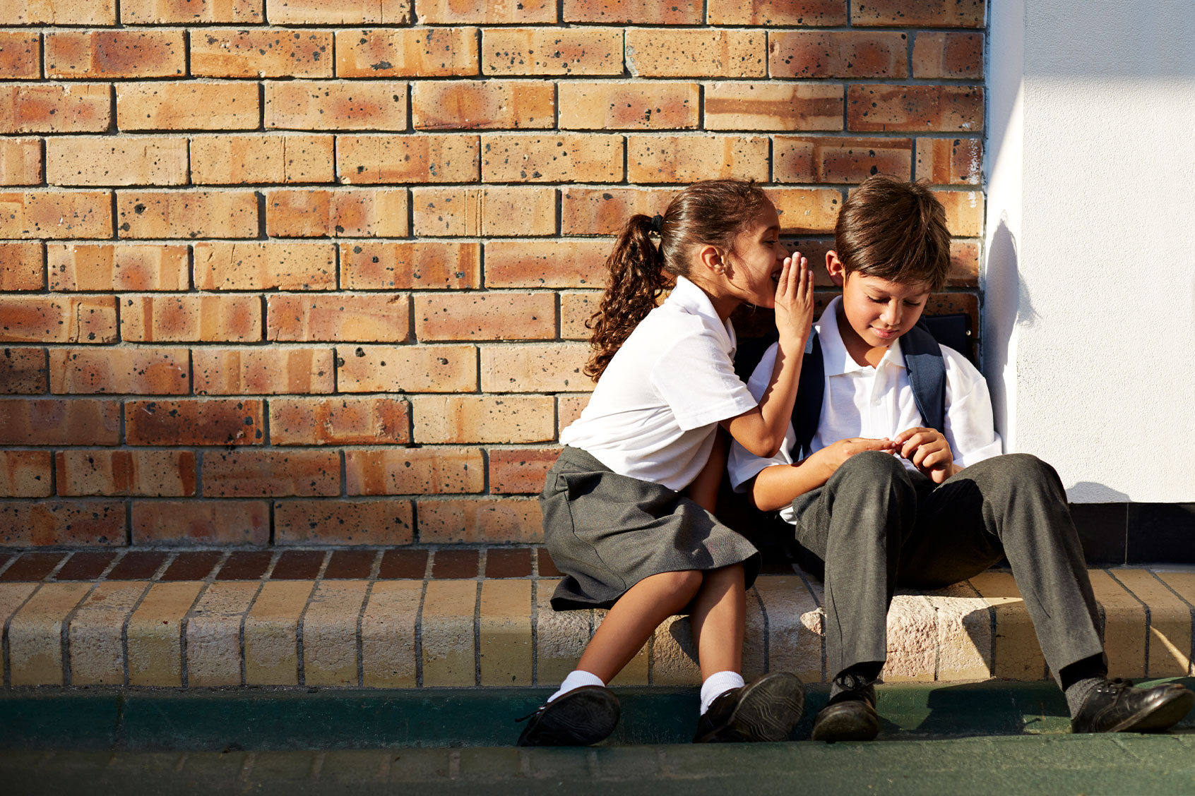 Schoolgirl whispering in classmates ear (Getty Images/Klaus Vedfelt)