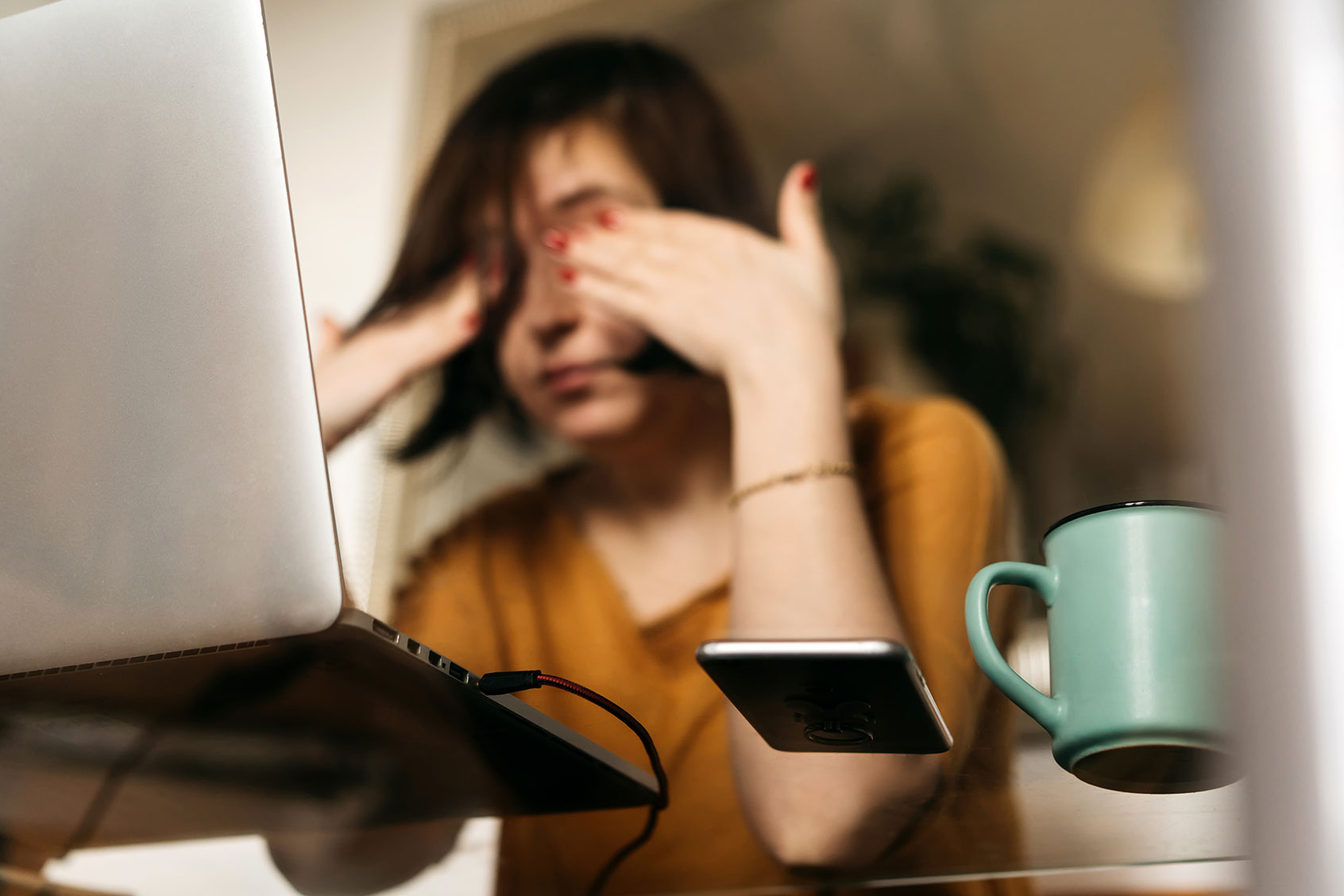 A woman sitting at a table working on her laptop, head in hands (Getty Images/Fiordaliso)