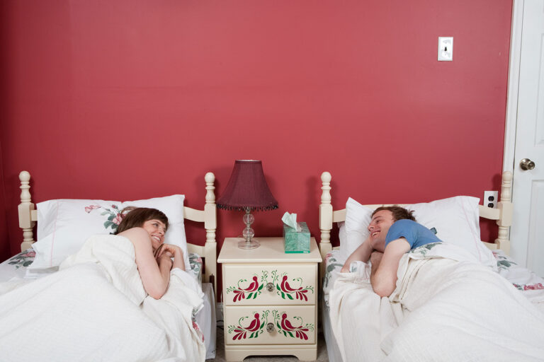 Young couple smiling at each other in single beds (Getty Images/Image Source)