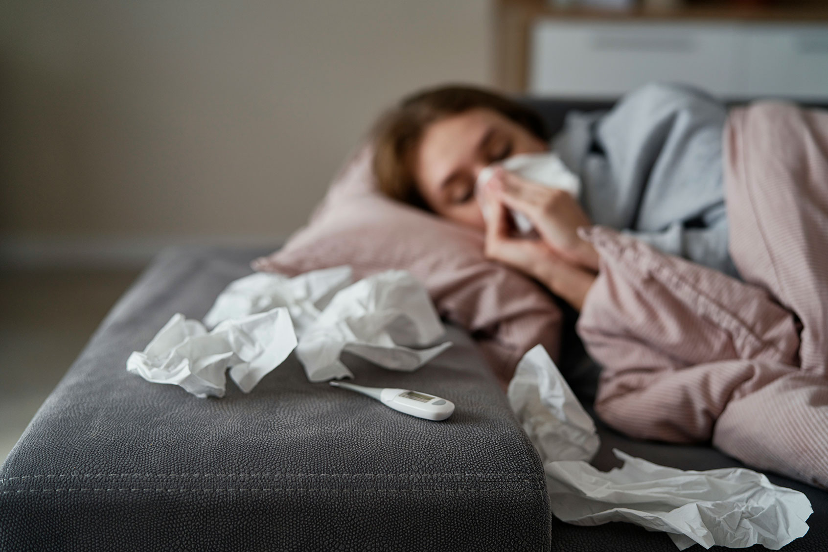 Young woman with high temperature and flu lying down on sofa (Getty Images/gpointstudio)