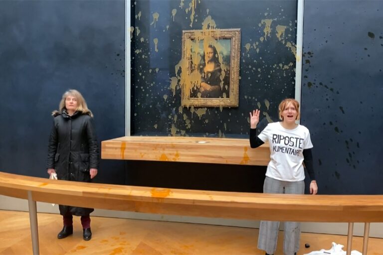 This image grab taken from AFPTV footage shows two environmental activists from the collective dubbed "Riposte Alimentaire" (Food Retaliation) gesturing as they stand in front of Leonardo Da Vinci's "Mona Lisa" (La Joconde) painting after hurling soup at the artwork, at the Louvre museum in Paris, on January 28, 2024. (DAVID CANTINIAUX/AFPTV/AFP via Getty Images)