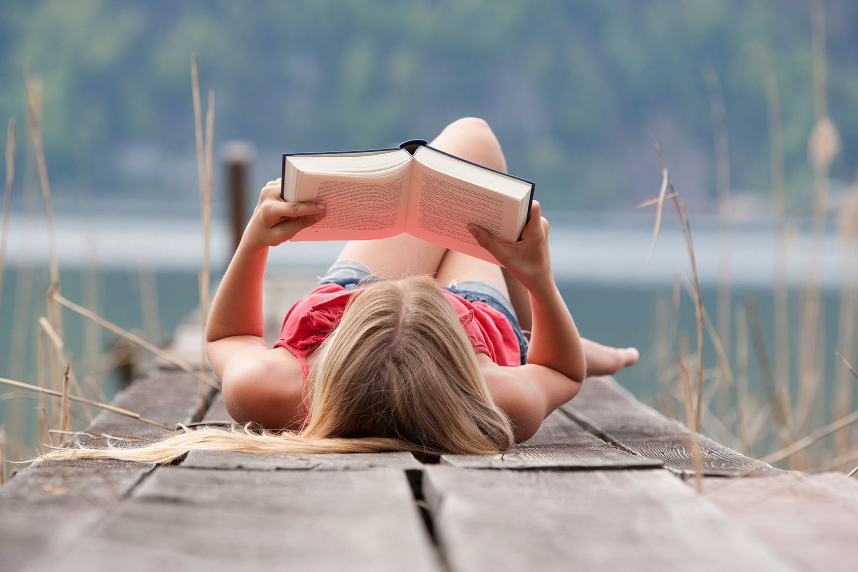 Woman lying and reading book on a jetty (Getty Images/Westend61)