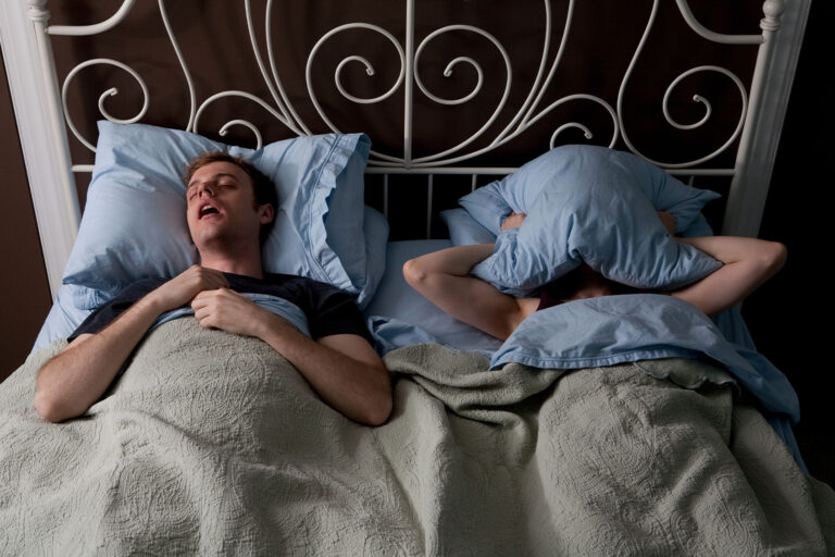 Young man snoring and woman covering face with pillow (Getty Images/Image Source)