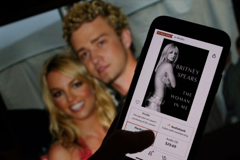This illustration image taken on October 21, 2023 shows the cover of Britney Spears' book "The Woman in Me" from an online retailer in front of a picture of Britney Spears and Justin Timberlake at the American Music Awards from January 9, 2002. ( CHRIS DELMAS/AFP via Getty Images)