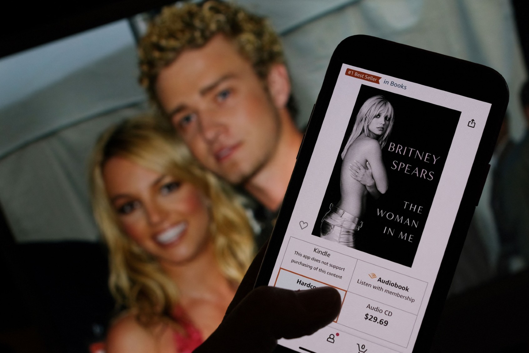 This illustration image taken on October 21, 2023 shows the cover of Britney Spears' book "The Woman in Me" from an online retailer in front of a picture of Britney Spears and Justin Timberlake at the American Music Awards from January 9, 2002. ( CHRIS DELMAS/AFP via Getty Images)