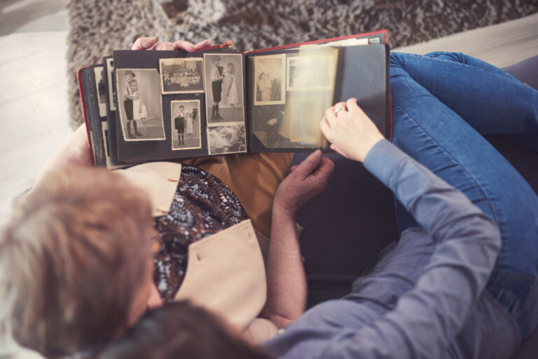 Young woman on sofa with grandmother looking at photo album (Getty Images/Gpointstudio)